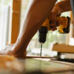 Close-up of a person using a power drill on wood indoors during daytime.